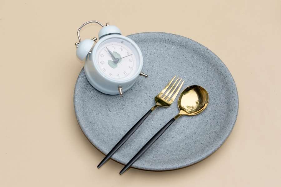 Assiette vide avec des couverts dorés et un réveil bleu posé dessus, symbolisant le respect des horaires dans le jeûne intermittent.